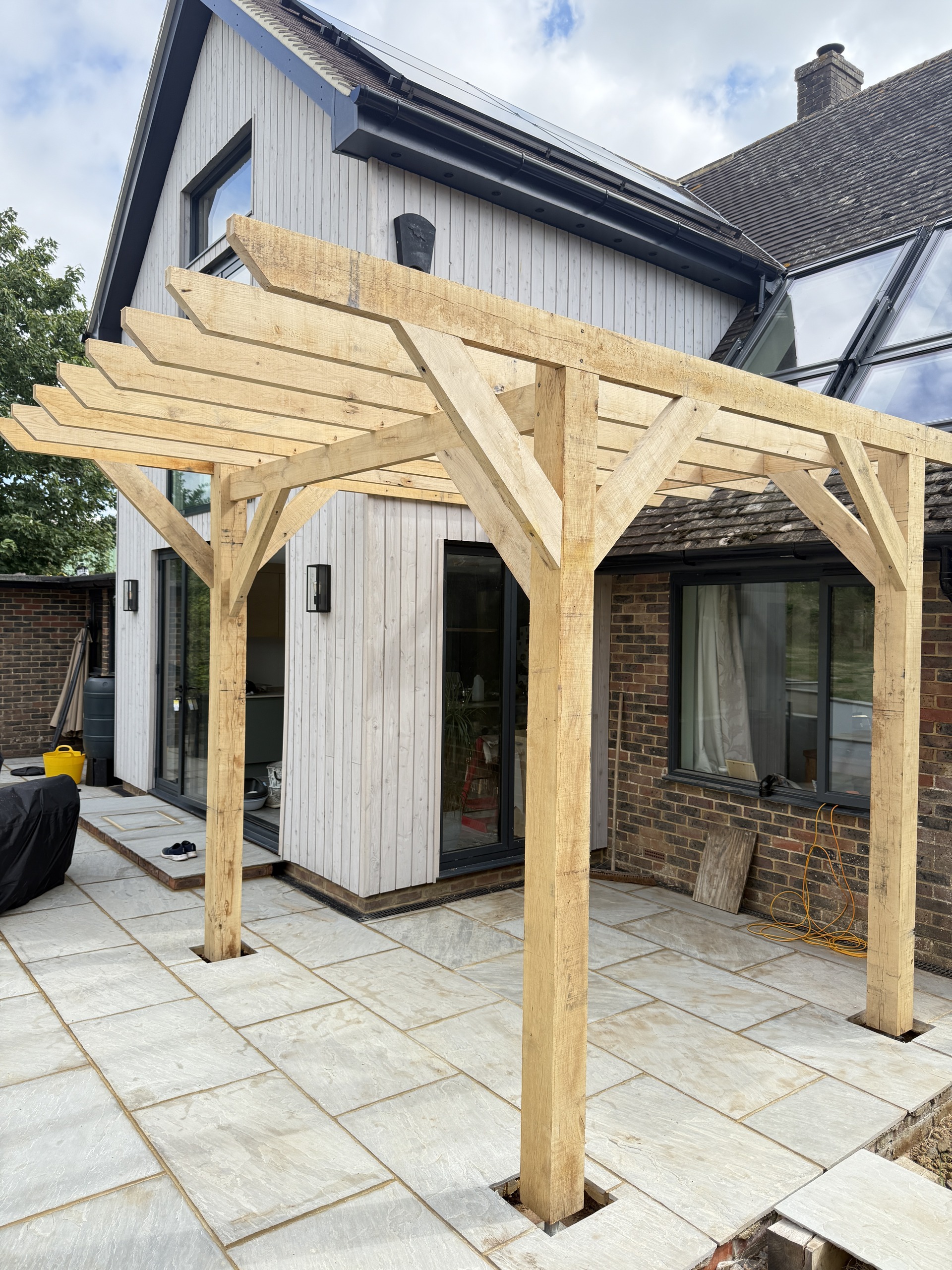 Green oak pergola showing braced posts, exposed beams and the patio setting
